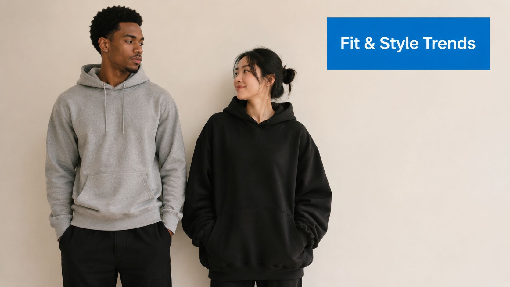 A young man and woman wearing comfortable gray and black hoodies standing against a neutral background.